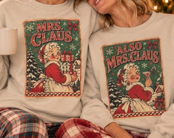 May include: Two beige crewneck sweatshirts featuring vintage-style illustrations of Mrs. Claus. One graphic reads MRS. CLAUS with a woman holding gifts, while the other reads ALSO MRS. CLAUS with a woman holding a cocktail glass.