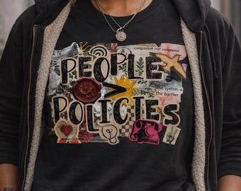 Puede incluir: Una camiseta negra con un gráfico de collage que incluye el texto "PEOPLE > POLICIES", "compassion over compliance" y "the system is the barrier". El diseño presenta un sello de cera rojo, un sol amarillo, un teléfono rosa y un signo de paz.