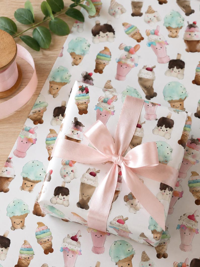 May include: A wrapped gift with a light pink satin bow. The wrapping paper is white and covered in colorful illustrations of smiling ice cream cones, sundaes, and milkshakes. A spool of pink ribbon is visible in the background.
