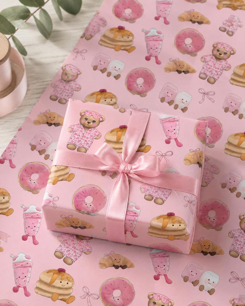 May include: A pink gift box wrapped in patterned paper featuring illustrations of donuts, pancakes, teddy bears, and milkshakes. The box is tied with a pink satin ribbon and bow. The background is a matching pink wrapping paper.