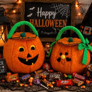 May include: Two plush orange pumpkin-shaped candy buckets with green fabric handles. One pumpkin features a classic jack-o'-lantern face with black eyes and a toothy grin, while the other has a smiling face with heart-shaped eyes and a green bow.