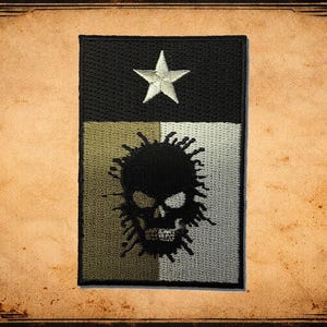 May include: A rectangular patch with a black top section featuring a white star. The lower section is divided into olive green and white squares. A black skull with spiky hair is centered on the lower section.