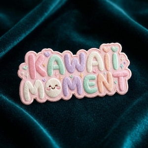 May include: A pastel-colored embroidered patch with the words "KAWAII MOMENT" in a whimsical font. The patch features a light pink background, with the text in shades of pink, green, purple, and orange. A smiling face is embroidered below the word "MOMENT".