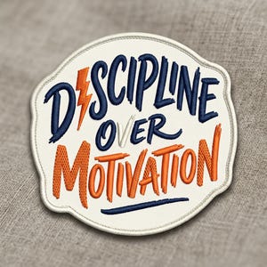 May include: Embroidered patch with the words "Discipline Over Motivation" in navy blue and orange. The patch has a white border and a lightning bolt graphic. The patch is on a gray fabric background.