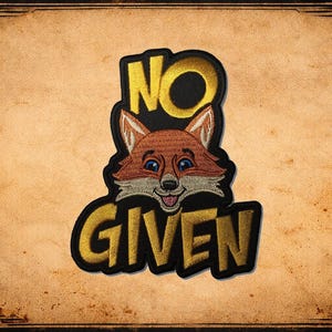 May include: Embroidered patch featuring a cartoon fox with the words "NO GIVEN" in gold lettering. The fox has orange fur, blue eyes, and a smiling expression. The patch is on a textured, tan background.