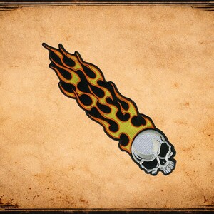 May include: Embroidered patch featuring a white skull with black eye sockets and a fiery trail of yellow, orange, and black flames. The patch is on a tan background with a decorative border.