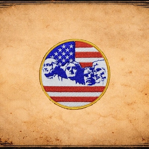 May include: Embroidered patch featuring the American flag with the faces of Mount Rushmore. The patch is circular with a gold border, set against a vintage, textured background with decorative corner elements.
