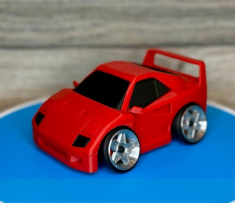 May include: A red toy car with black windows and silver wheels. The car has a spoiler and a low profile. The toy car is sitting on a blue surface.