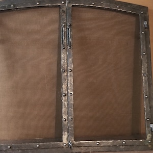 Peut inclure: Une paire de portes de cheminée en métal noir avec un dessus arrondi et une grille en maille. Les portes ont une finition martelée et sont fixées par des rivets.