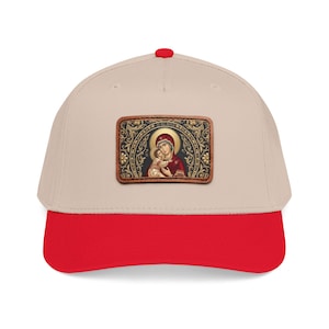 Op de afbeelding: Beige baseballpet met een rode klep en een rode knop. De pet heeft een rechthoekige patch met een religieus icoon van een vrouw die een kind vasthoudt, omringd door sierlijke gouden details.