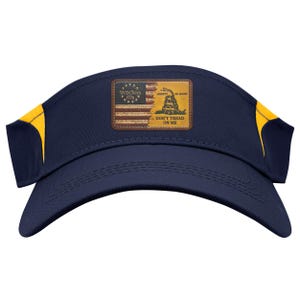 Pode incluir: Viseira azul marinho com detalhes amarelos. Um patch retangular apresenta uma bandeira americana desgastada e uma cobra amarela com o texto "Liberty or Death" e "Don't Tread on Me". A viseira foi projetada para proteger os olhos do sol.