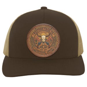 May include: A brown baseball cap with a tan mesh back and a circular leather patch on the front. The patch features a steer skull, crossed revolvers, a horseshoe, and cacti with the text Western Trail Co. Legendary Goods Est. 1873.