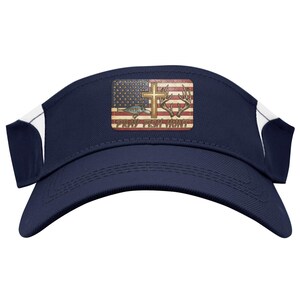 May include: Navy blue visor with white side accents. It has a rectangular patch with an American flag design, a cross, deer antlers, and the text "Pray Fish Hunt".