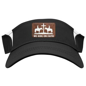 May include: Black visor with white accents and a curved brim. A brown patch features a cross and riders on horseback, with the text "WE RIDE ON FAITH". The visor is designed to shield the eyes from the sun.