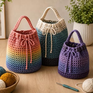May include: Three crochet bucket bags with drawstring closures and single top handles. One bag features a rainbow gradient, one has a cream top with a teal and dark gray base, and one displays a purple gradient. Each bag has a grid-like texture.