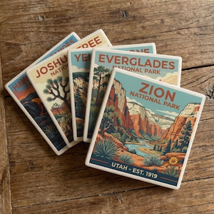 May include: A collection of ceramic coasters featuring national park designs. Each coaster displays a different park, including Zion, Everglades, and Joshua Tree, with vibrant illustrations and text. The coasters are arranged on a wooden surface.