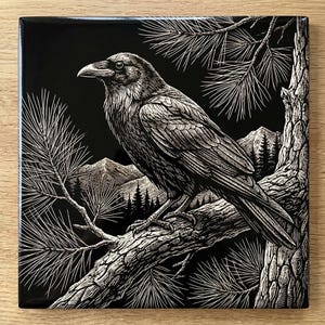 May include: A black square tile featuring a detailed white illustration of a raven perched on a tree branch. The artwork includes pine needles, mountains, and a forest, creating a nature-themed design. The raven is the focal point, with intricate feather and branch details.