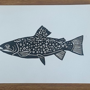 May include: A black and white linocut print of a fish. The fish has a detailed design with spots and fins. The print is on white paper.