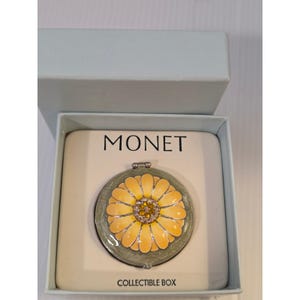 May include: A round Monet compact mirror featuring a yellow daisy design with a crystal-encrusted center on a sage green background. The item is presented in a light blue box with the text MONET and COLLECTIBLE BOX printed on the insert.