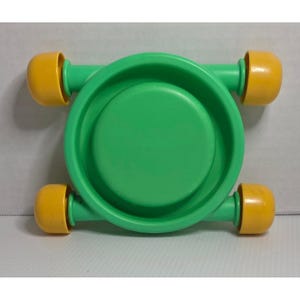 Puede incluir: Un monopatín de juguete verde y amarillo con una base circular y cuatro ruedas amarillas. El juguete está hecho de plástico y está diseñado para niños pequeños. El monopatín es de color verde vibrante con ruedas amarillas.