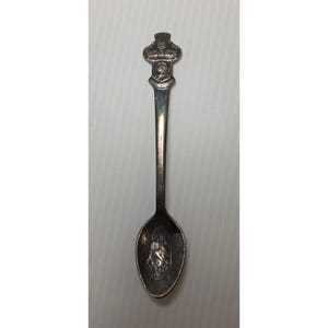 May include: A silver-coloured souvenir spoon with an intricate design. The handle displays the word "ROLEX" above a crest. The spoon's bowl has an embossed image. A collectible item.