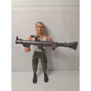Könnte beinhalten: Eine Kunststoff-Actionfigur eines Mannes in einem weißen Tanktop und Camouflage-Hose, der einen grauen Raketenwerfer hält. Die Figur hat schwarze Stiefel und einen neutralen Gesichtsausdruck.