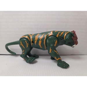 Peut inclure: Figurine de jouet tigre vert et orange. Le tigre jouet a des rayures orange et une tête brun-rouge. Le jouet est en plastique et a une queue. Le jouet est en position de marche.