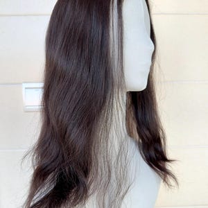 May include: A dark brown wig with long, wavy hair is displayed on a white mannequin head. The wig features a natural-looking hairline and a side part. The hair has a slight sheen and appears to be layered, creating volume and movement.