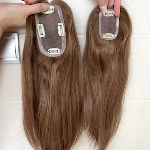 May include: Two light brown hair toppers with straight, smooth strands. Each piece features a sheer base with multiple small metal pressure-sensitive clips attached to the underside for secure placement, showing the construction of the hair extensions.