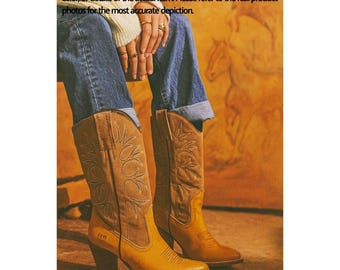 May include: A pair of tan leather cowboy boots with decorative stitching and a pointed toe. The boots have a high heel and are worn with blue jeans. The text "FRYE" is visible on the side of one boot.