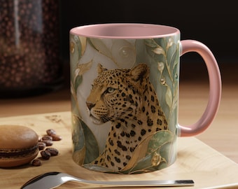 May include: A ceramic mug with a soft pink interior and handle, featuring a detailed illustration of a leopard surrounded by stylised green leaves and gold accents. The exterior surface displays a smooth finish with a wrap-around animal print design.