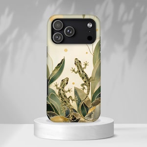 Op de afbeelding: Een smartphonehoesje met een decoratieve illustratie van twee gekko's die tussen gestileerde groene en gouden bladeren klimmen. Het ontwerp bevat geometrische patronen, dunne gouden lijnen en kleine gouden cirkels op een crèmekleurige achtergrond.