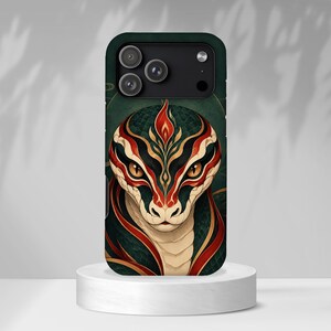 May include: A smartphone case featuring a detailed illustration of a snake head with scales in shades of dark green, cream, and vibrant red. The snake has piercing amber eyes and a flame-like pattern on its forehead, set against a dark green background.