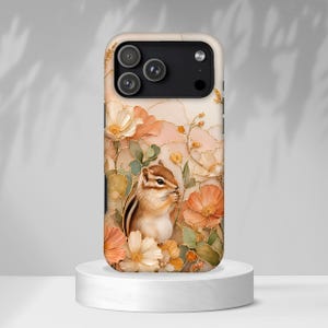 Puede incluir: Una funda para smartphone con una ardilla listada rodeada de flores color melocotón, crema y verde salvia con vetas doradas. El diseño incluye un recorte negro para el módulo de cámara en la parte superior, sobre un fondo suave y jaspeado.