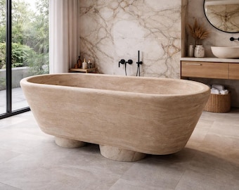 May include: A beige, oval-shaped bathtub with a rounded design, set on three circular feet. The bathroom features a marble wall, a large window, and a wooden vanity with a round mirror.