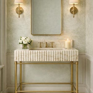 Pu&ograve; includere: Un lussuoso mobile da bagno con lavabo in marmo e finiture dorate. Il lavabo presenta un design scanalato e poggia su una struttura in metallo dorato. Uno specchio rettangolare e due applique sono visibili.
