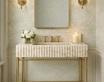 May include: A luxurious bathroom vanity with a marble sink and gold fixtures. The sink has a ribbed design and sits atop a gold metal frame. A rectangular mirror and two sconces with cream-colored shades are mounted on the wall above the sink.