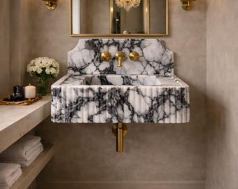 May include: A luxurious bathroom interior featuring a marble sink with gold fixtures. The sink has a black and white veined pattern. A gold-framed mirror hangs above the sink, and sconces flank the mirror. A shelf with towels and a tray with candles is visible.