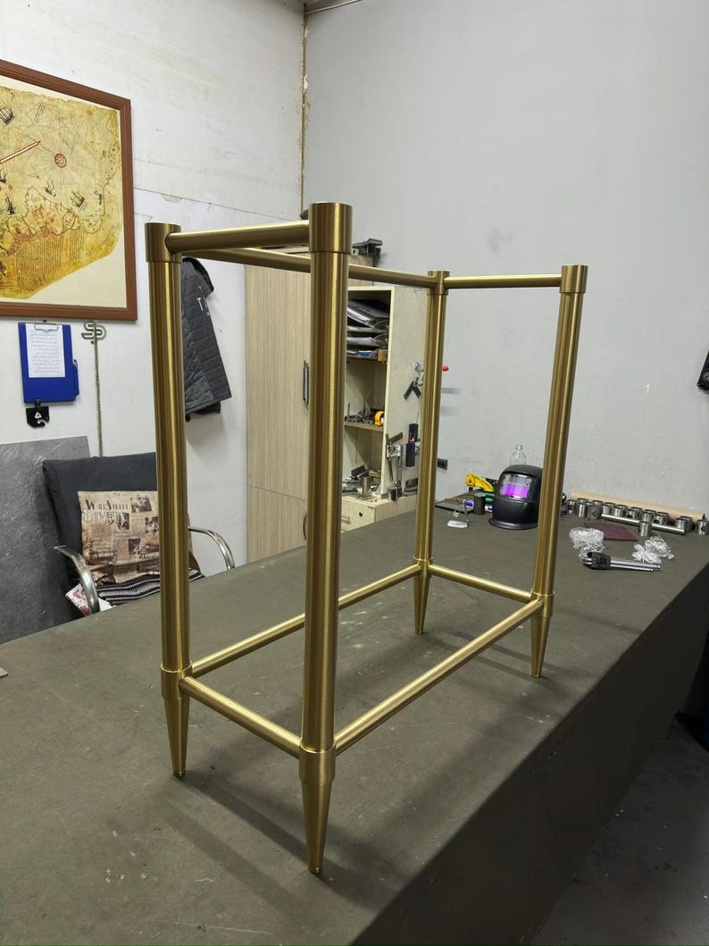 Pu&ograve; includere: Un telaio in metallo color oro con un design rettangolare. Il telaio ha quattro gambe e barre orizzontali, creando una struttura simile a uno scaffale. Le gambe sono affusolate e il design generale &egrave; minimalista.