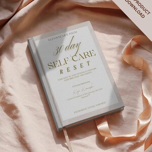 Könnte beinhalten: Ein Hardcover-Buch mit dem Titel "30 Day Self Care Reset" mit goldfarbenen Buchstaben und einem hellgrauen Einband. Das Buch enthält Text zur Wiederherstellung von Geist und Körperenergie. Ein pfirsichfarbenes Band und die Worte "Digital Product PDF Download" sind ebenfalls sichtbar.