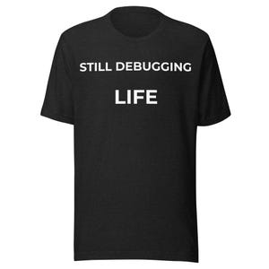 Op de afbeelding: Zwart t-shirt met de witte tekst "STILL DEBUGGING LIFE". Het shirt heeft een ronde hals en korte mouwen. De stof lijkt een zacht, gemêleerd materiaal te zijn.