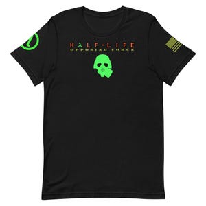 Puede incluir: Camiseta negra con el texto "HALF-LIFE OPPOSING FORCE" en rojo y verde. Un gráfico de máscara de gas verde está centrado debajo del texto. Un símbolo verde está en la manga izquierda y una bandera estadounidense en la manga derecha.