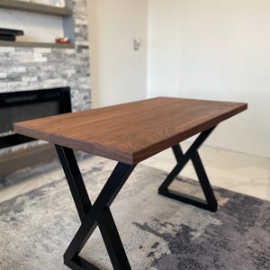 May include: A rectangular wooden table with a dark brown surface. The table is supported by black metal legs in an X-shape design. The table appears to be approximately 60 inches long.