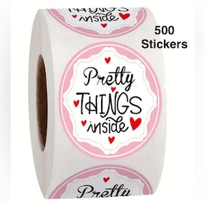 May include: A roll of white stickers with a pink and white border design. The stickers have the words "Pretty Things Inside" in black script with red heart accents. The roll contains 500 stickers.