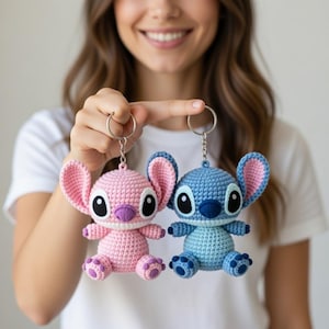 Può includere: Due portachiavi all'uncinetto, uno rosa e uno blu, ciascuno con un design di personaggi dei cartoni animati con grandi orecchie e grandi occhi. I portachiavi sono tenuti da una persona. Il portachiavi rosa ha accenti viola, mentre quello blu ha accenti blu scuro.