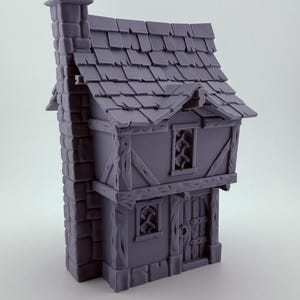 May include: A miniature, grey fantasy cottage with a chimney, tiled roof, and two storeys. The cottage features detailed wooden beams, small windows, and a front door with a round handle. The overall design evokes a medieval or fairytale aesthetic.