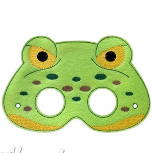 Puede incluir: Máscara de rana de fieltro verde con ojos amarillos y manchas marrones. La máscara tiene dos agujeros para los ojos del usuario.