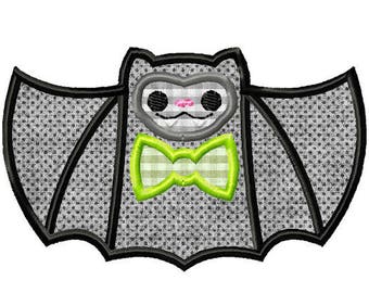 Puede incluir: Un murciélago negro y gris con una pajarita verde. El murciélago tiene una cara de dibujos animados linda con mejillas rosadas y una pequeña boca.