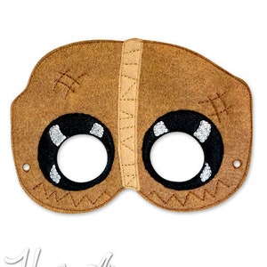 Puede incluir: Una máscara de fieltro marrón con detalles cosidos y dos agujeros para los ojos. La máscara tiene forma de cara con ojos cosidos y una boca cosida.