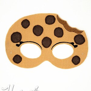 May include: A brown felt cookie mask with chocolate chips and a bite taken out of it. The mask has eye holes and is designed for children's play.